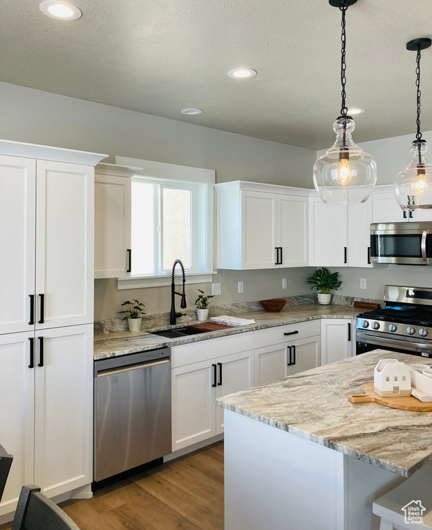 Kitchen featuring stainless steel appliances, light stone countertops, decorative light fixtures, and white cabinetry