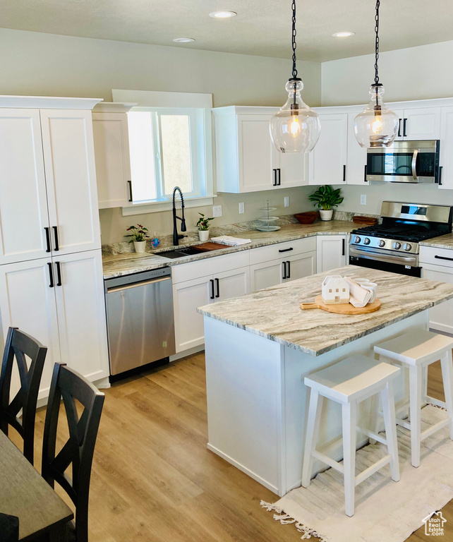 Kitchen featuring light stone counters, hanging light fixtures, appliances with stainless steel finishes, light hardwood / wood-style flooring, and white cabinets