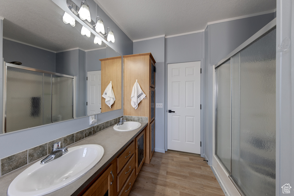 Bathroom with hardwood / wood-style floors, a shower with door, dual bowl vanity, ornamental molding, and a textured ceiling