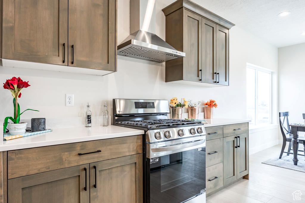Kitchen featuring stainless steel gas range, wall chimney range hood, and light wood-type flooring
