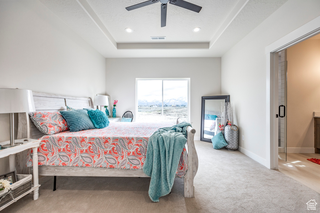 Carpeted bedroom with a textured ceiling, ceiling fan, and a raised ceiling