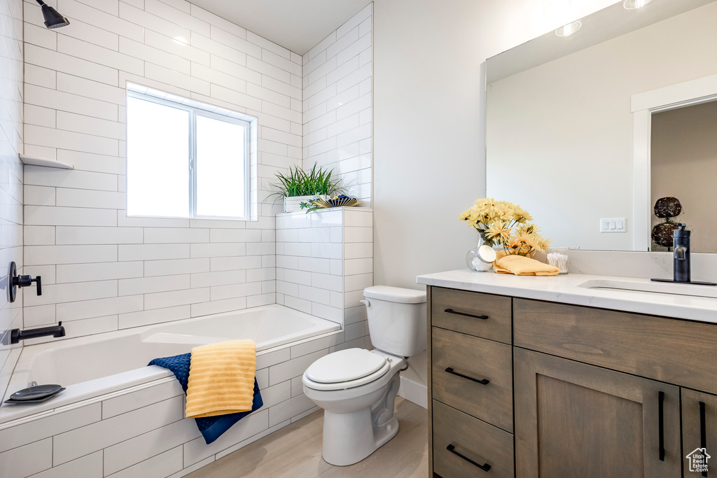 Full bathroom with tiled shower / bath combo, toilet, vanity, and hardwood / wood-style floors