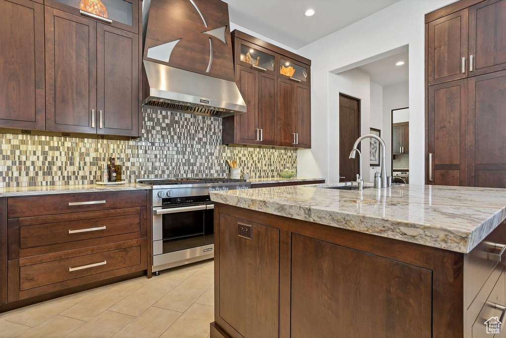 Kitchen featuring wall chimney exhaust hood, stainless steel gas range, light stone countertops, and backsplash