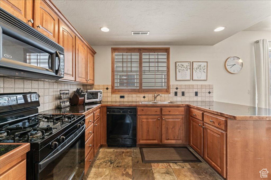 Kitchen with backsplash, kitchen peninsula, sink, black appliances, and dark tile flooring
