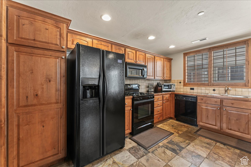 Kitchen with tasteful backsplash, black appliances, sink, and dark tile floors