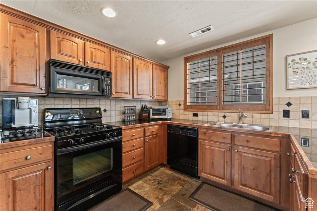 Kitchen with backsplash, sink, black appliances, and dark tile floors