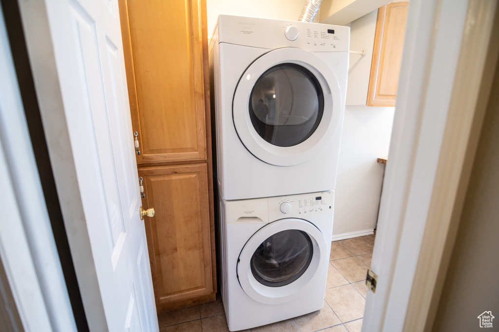 Washroom featuring cabinets, light tile floors, and stacked washer and clothes dryer