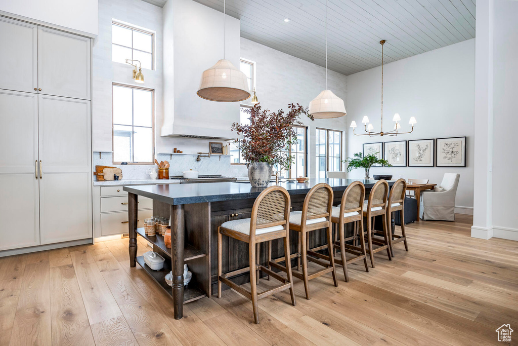 Kitchen with decorative light fixtures, light hardwood / wood-style flooring, a high ceiling, a breakfast bar, and a chandelier