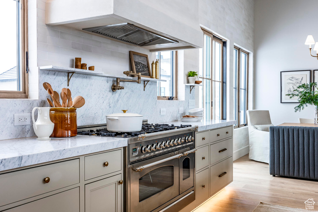 Kitchen featuring range with two ovens, backsplash, radiator heating unit, custom exhaust hood, and light wood-type flooring