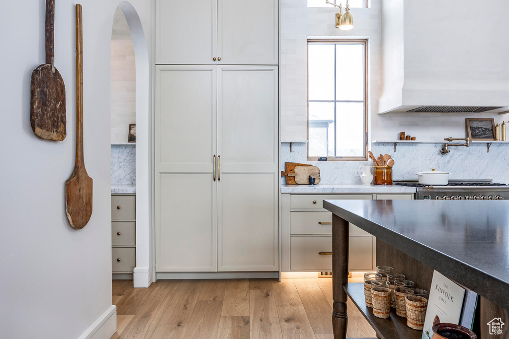 Kitchen featuring tasteful backsplash, custom range hood, white cabinetry, and light wood-type flooring