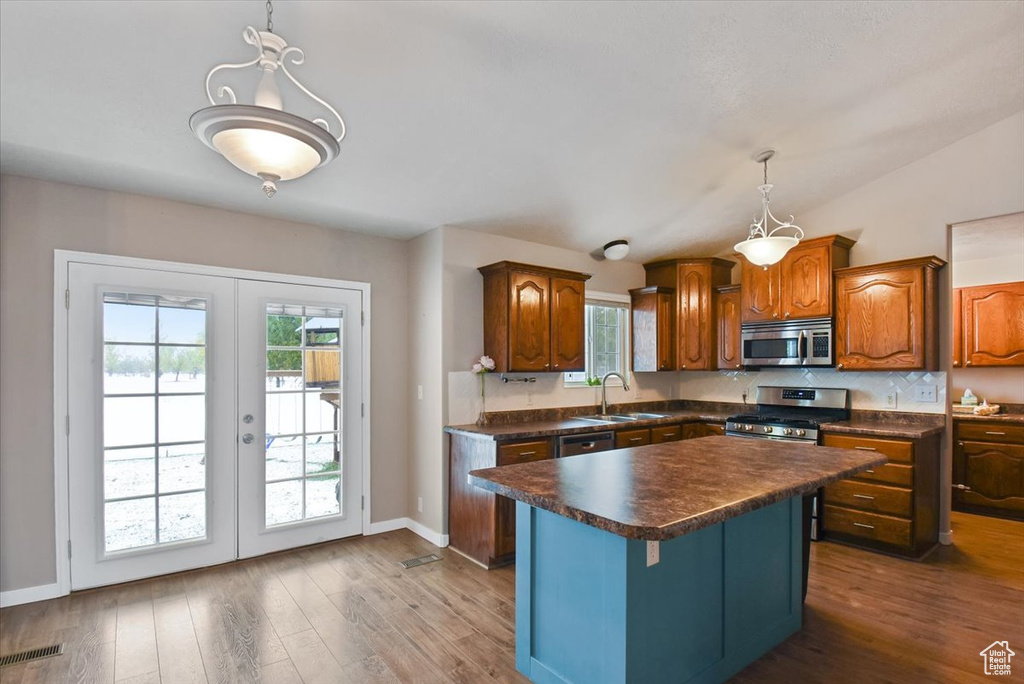 Kitchen with hanging light fixtures, stainless steel appliances, a kitchen island, and a healthy amount of sunlight