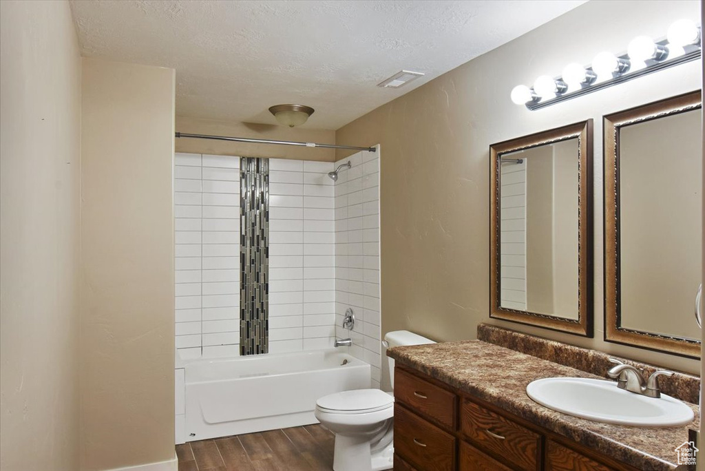 Full bathroom with toilet, vanity, hardwood / wood-style flooring, tiled shower / bath combo, and a textured ceiling