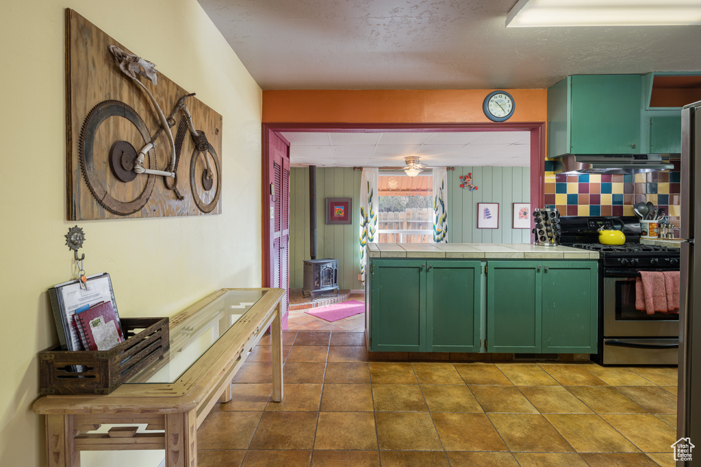 Kitchen featuring tile counters, wall chimney exhaust hood, stainless steel gas range, dark tile flooring, and tasteful backsplash