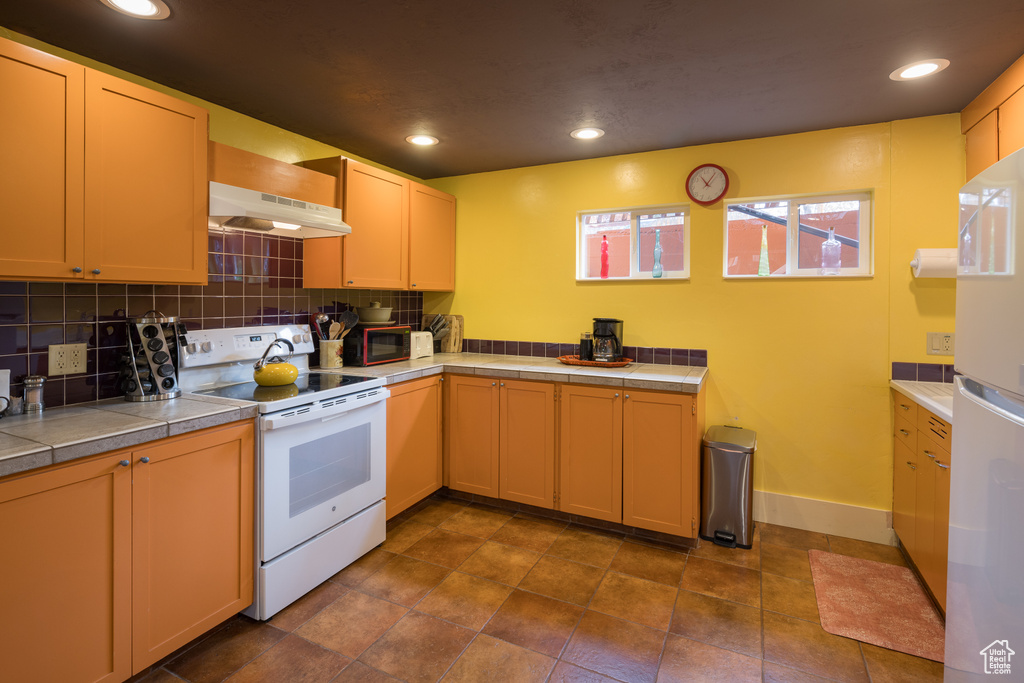 Kitchen with dark tile floors, tile countertops, white appliances, and backsplash