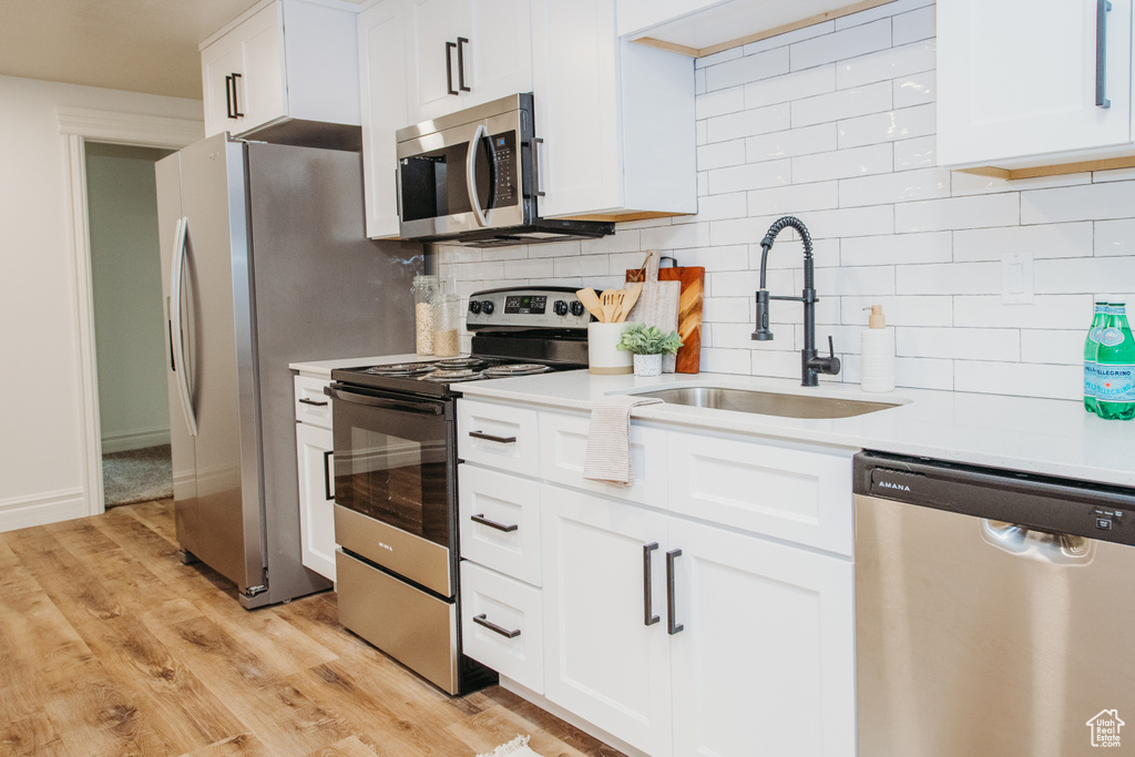 Kitchen featuring stainless steel appliances, tasteful backsplash, white cabinetry, and light hardwood / wood-style flooring