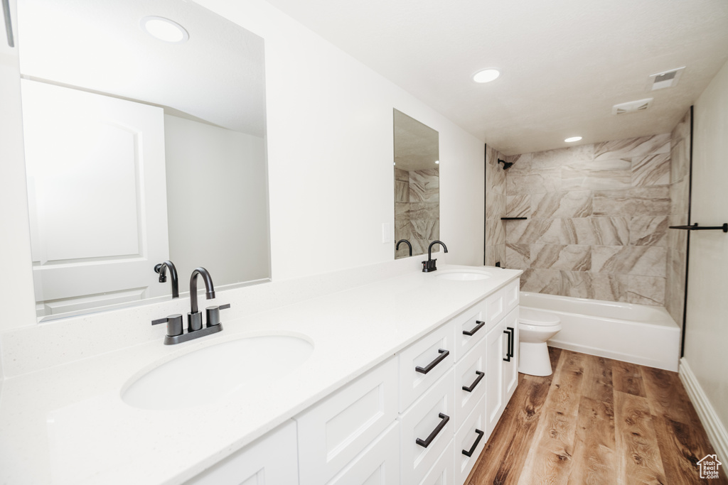 Full bathroom with toilet, dual vanity, tiled shower / bath combo, and hardwood / wood-style flooring