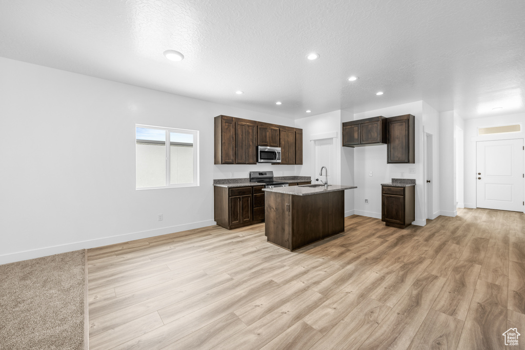 Kitchen featuring light hardwood / wood-style floors, appliances with stainless steel finishes, a kitchen island with sink, and dark brown cabinetry