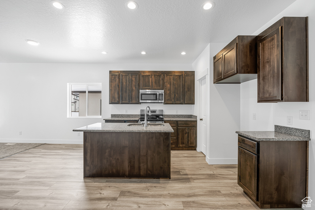 Kitchen featuring dark stone countertops, appliances with stainless steel finishes, light hardwood / wood-style flooring, sink, and a kitchen island with sink