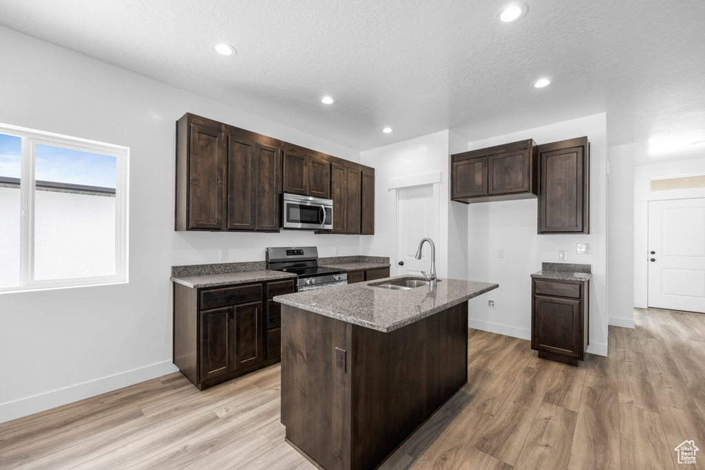 Kitchen with sink, appliances with stainless steel finishes, an island with sink, and light hardwood / wood-style flooring