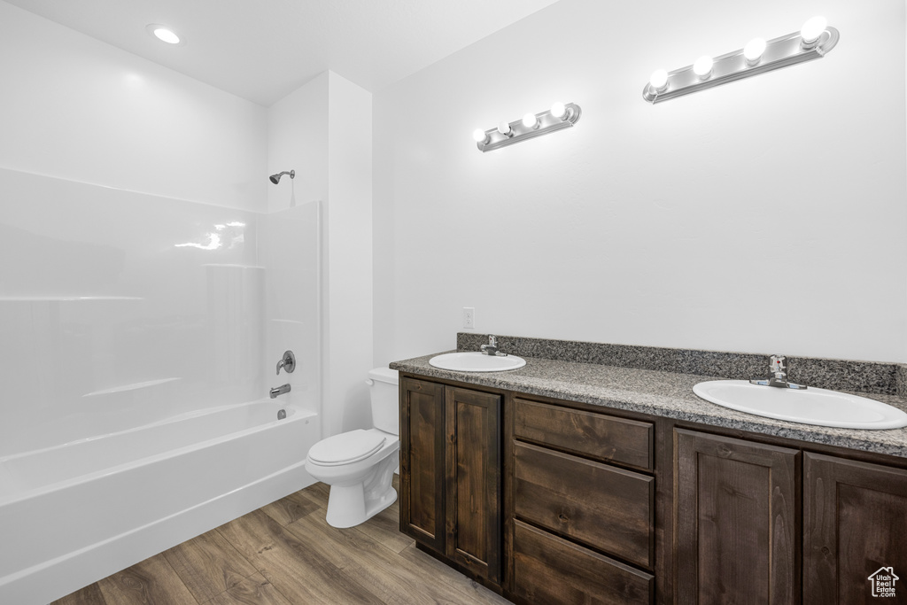 Full bathroom with wood-type flooring, toilet, washtub / shower combination, and double vanity