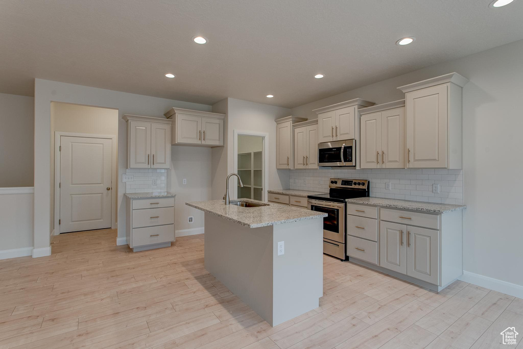 Kitchen featuring a kitchen island with sink, sink, stainless steel appliances, and backsplash