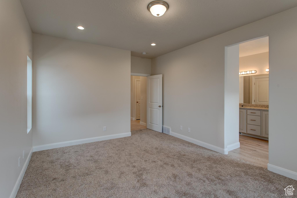 Unfurnished bedroom with ensuite bathroom and light carpet