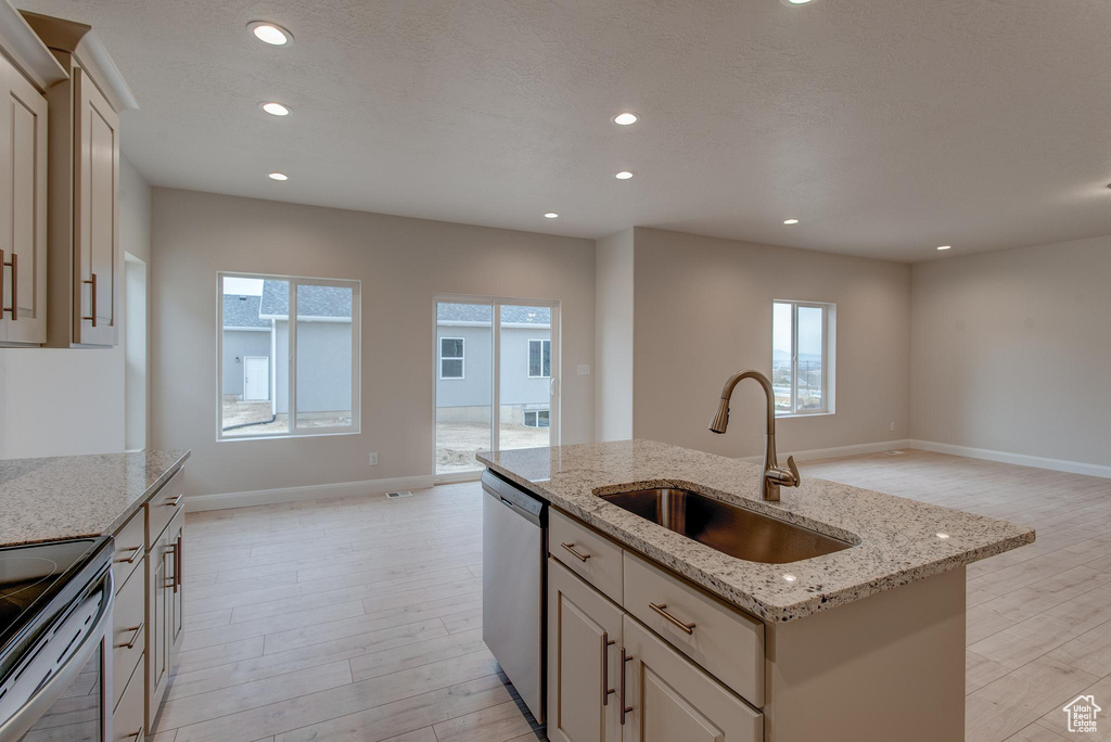 Kitchen with light hardwood / wood-style floors, light stone counters, a center island with sink, dishwasher, and sink