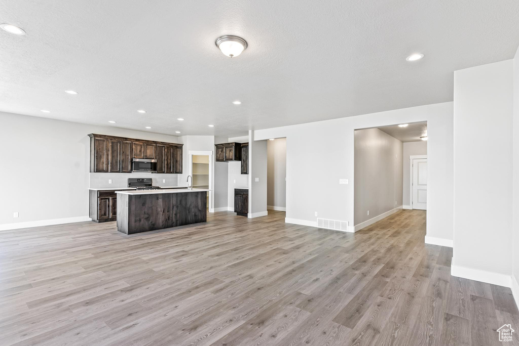 Kitchen with light wood-type flooring, dark brown cabinets, an island with sink, and range