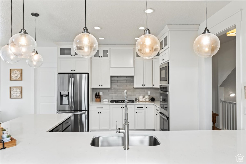 Kitchen with tasteful backsplash, decorative light fixtures, white cabinets, sink, and stainless steel appliances