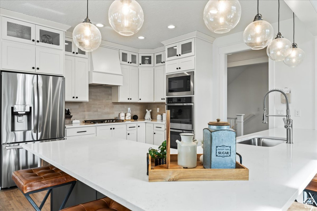 Kitchen with white cabinetry, premium range hood, appliances with stainless steel finishes, backsplash, and sink