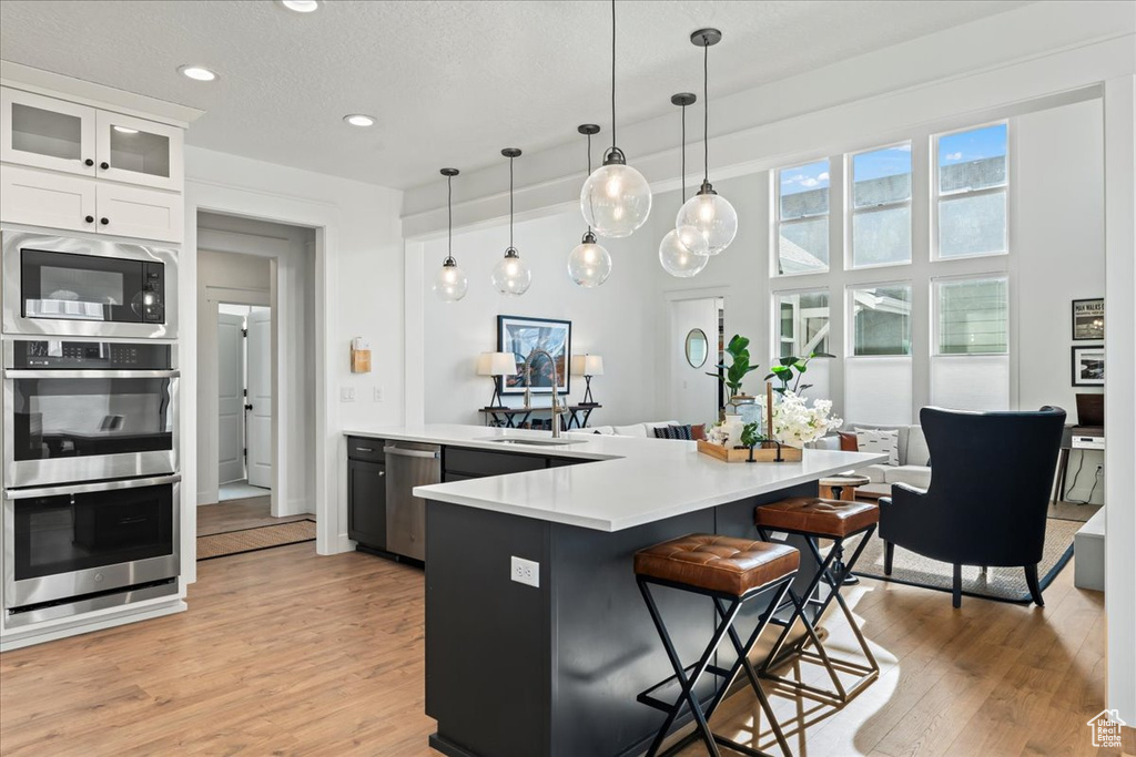 Kitchen with a breakfast bar area, hanging light fixtures, appliances with stainless steel finishes, light wood-type flooring, and white cabinetry