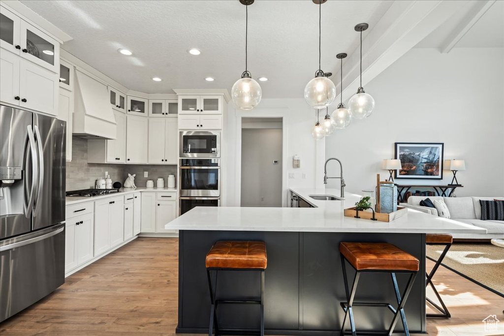 Kitchen with a kitchen bar, appliances with stainless steel finishes, premium range hood, light wood-type flooring, and tasteful backsplash