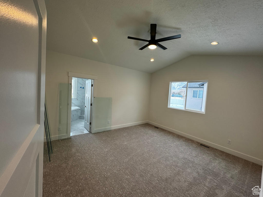 Carpeted empty room featuring lofted ceiling, a textured ceiling, and ceiling fan