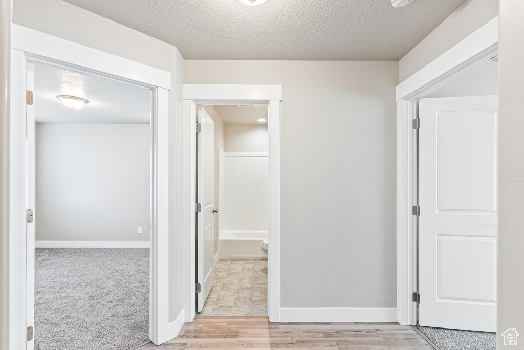 Hallway with a textured ceiling and light colored carpet