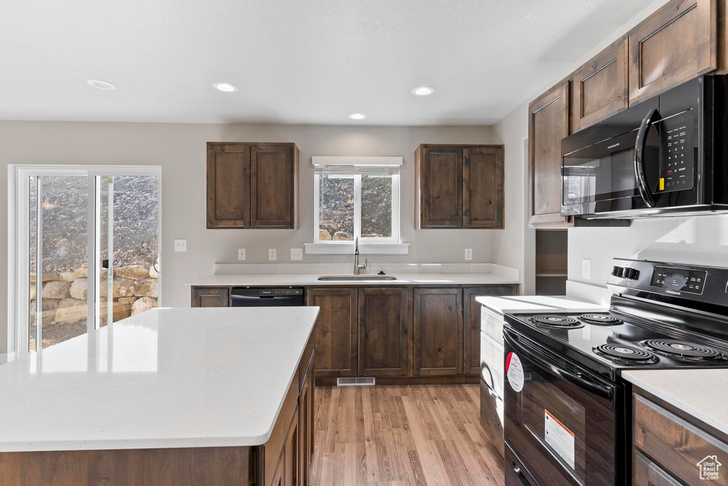 Kitchen featuring black appliances, light hardwood / wood-style floors, dark brown cabinetry, sink, and a kitchen island