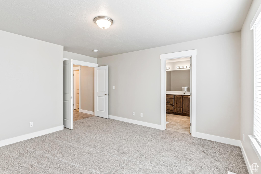 Unfurnished bedroom with ensuite bathroom, multiple windows, and light carpet