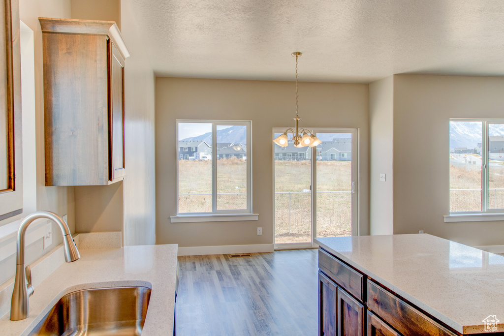 Kitchen featuring hanging light fixtures, a chandelier, wood-type flooring, light stone counters, and sink