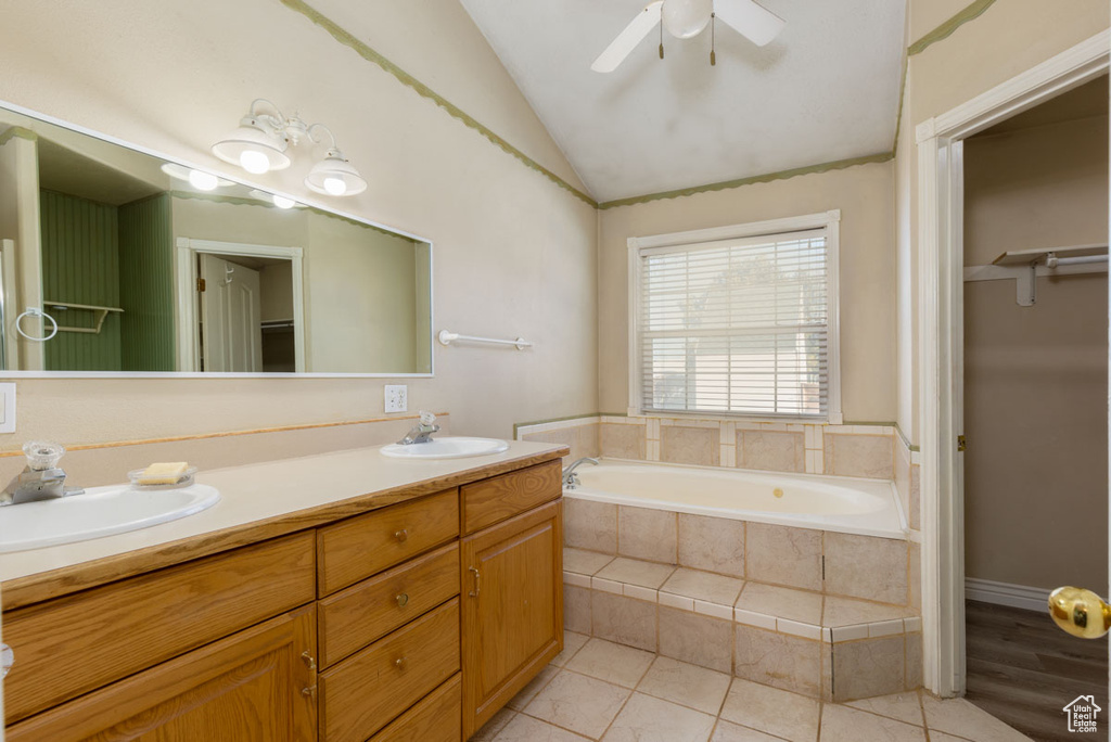 Bathroom featuring ceiling fan, tiled tub, lofted ceiling, tile floors, and double vanity