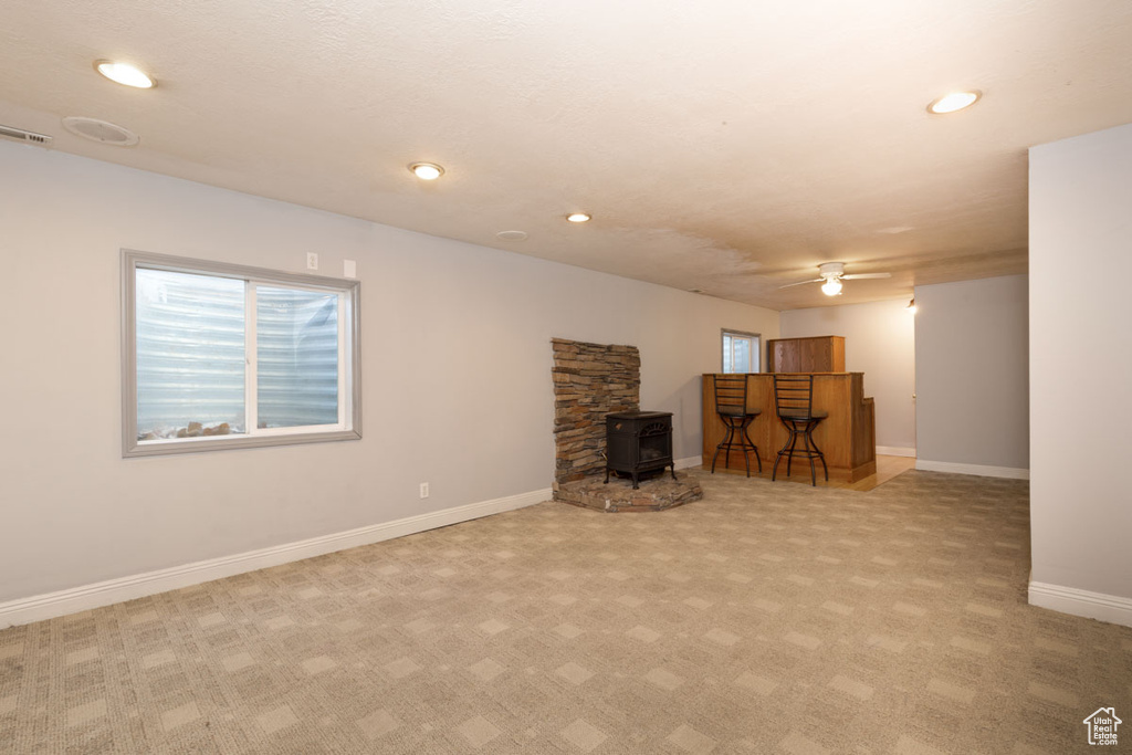 Basement with a wealth of natural light, a wood stove, light carpet, and ceiling fan