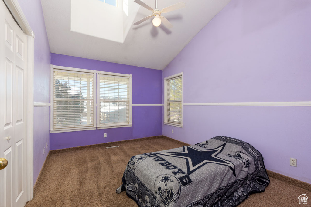 Carpeted bedroom with a closet, lofted ceiling, multiple windows, and ceiling fan