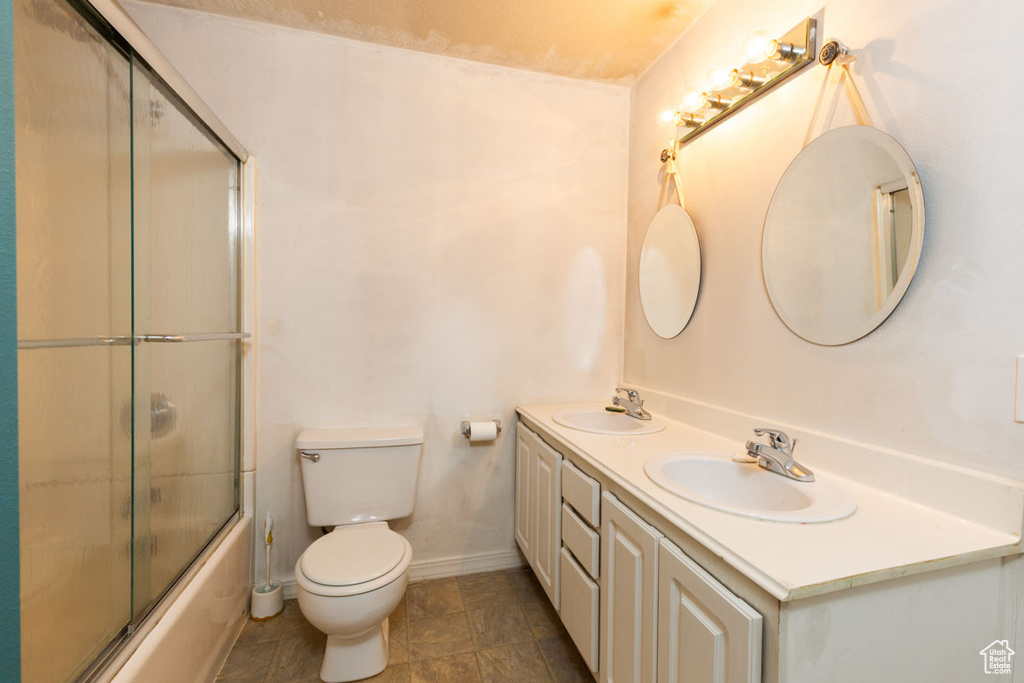 Full bathroom featuring double vanity, toilet, tile flooring, and combined bath / shower with glass door