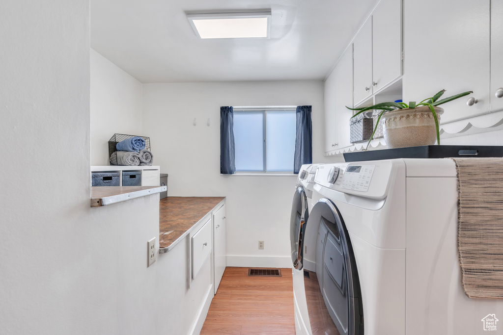 Washroom with washer and clothes dryer, light hardwood / wood-style floors, and cabinets