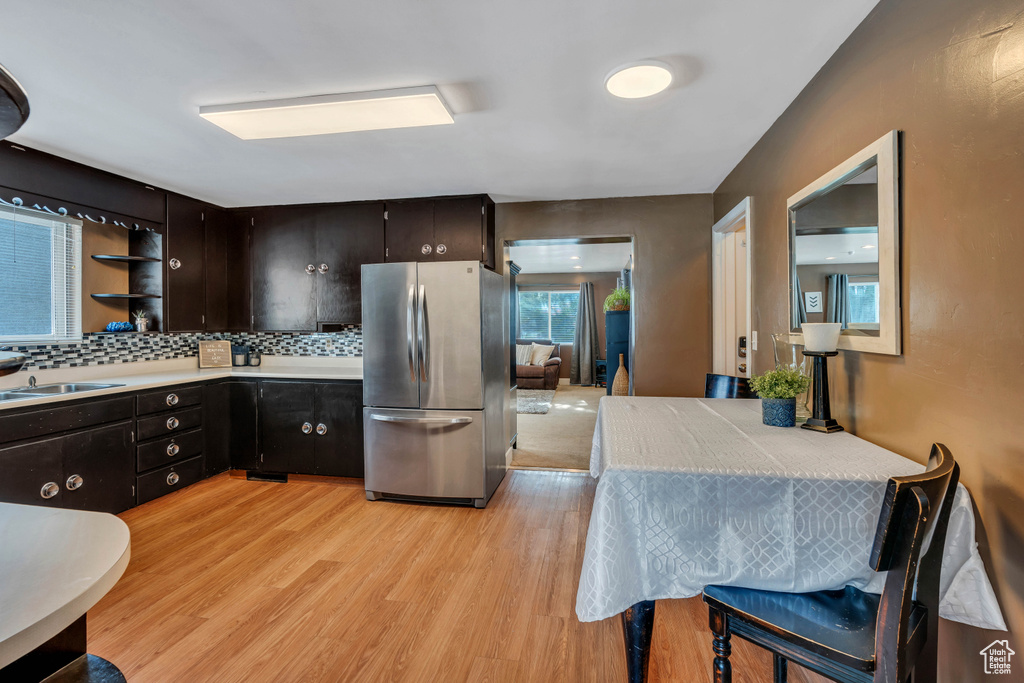 Kitchen featuring sink, backsplash, light wood-type flooring, dark brown cabinets, and stainless steel fridge