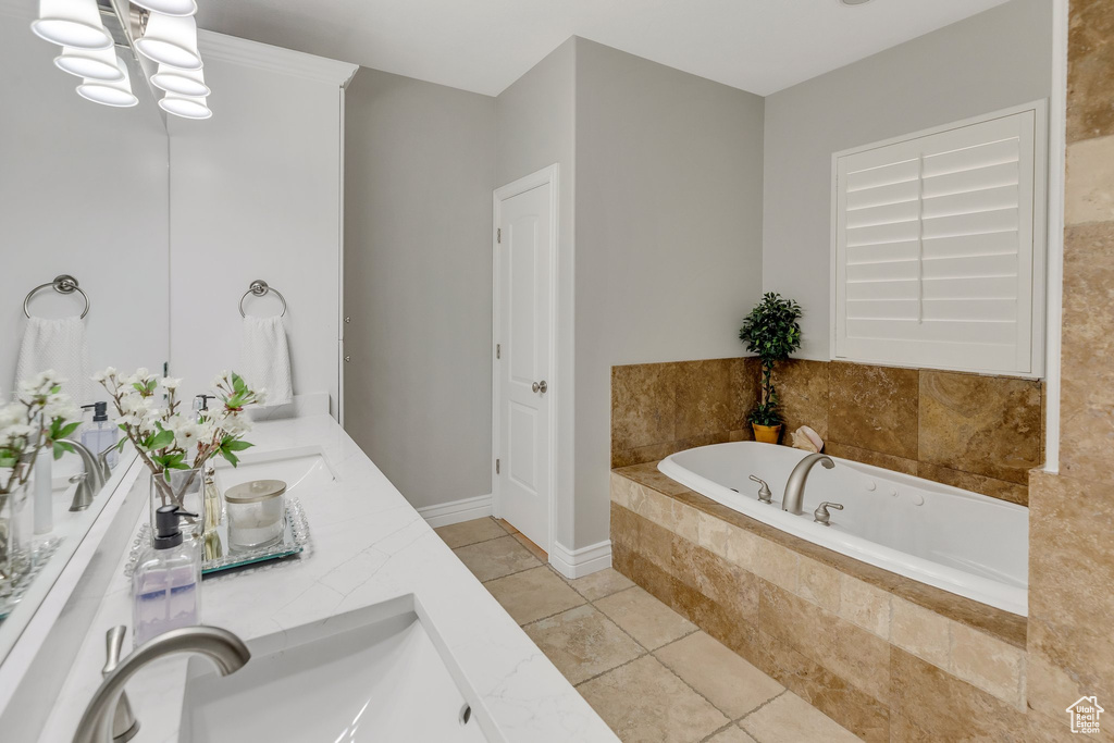 Bathroom featuring tile floors, a relaxing tiled bath, a notable chandelier, and dual bowl vanity