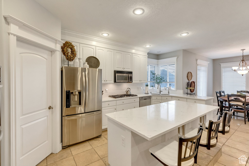 Kitchen with a breakfast bar, a chandelier, appliances with stainless steel finishes, decorative light fixtures, and white cabinets