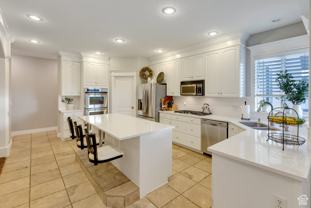 Kitchen featuring a kitchen bar, a center island, stainless steel appliances, sink, and white cabinetry