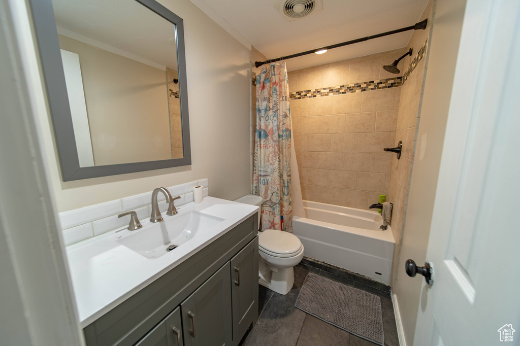 Full bathroom featuring toilet, tile floors, vanity with extensive cabinet space, shower / bath combo with shower curtain, and ornamental molding