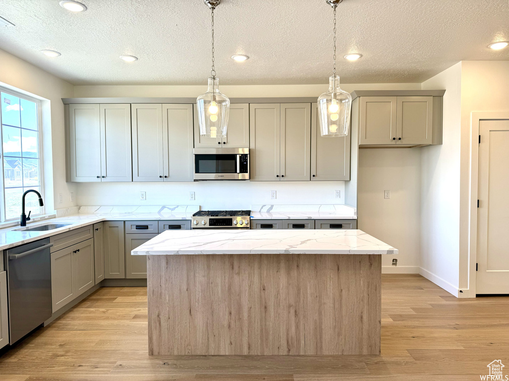 Kitchen with sink, appliances with stainless steel finishes, decorative light fixtures, and light hardwood / wood-style flooring