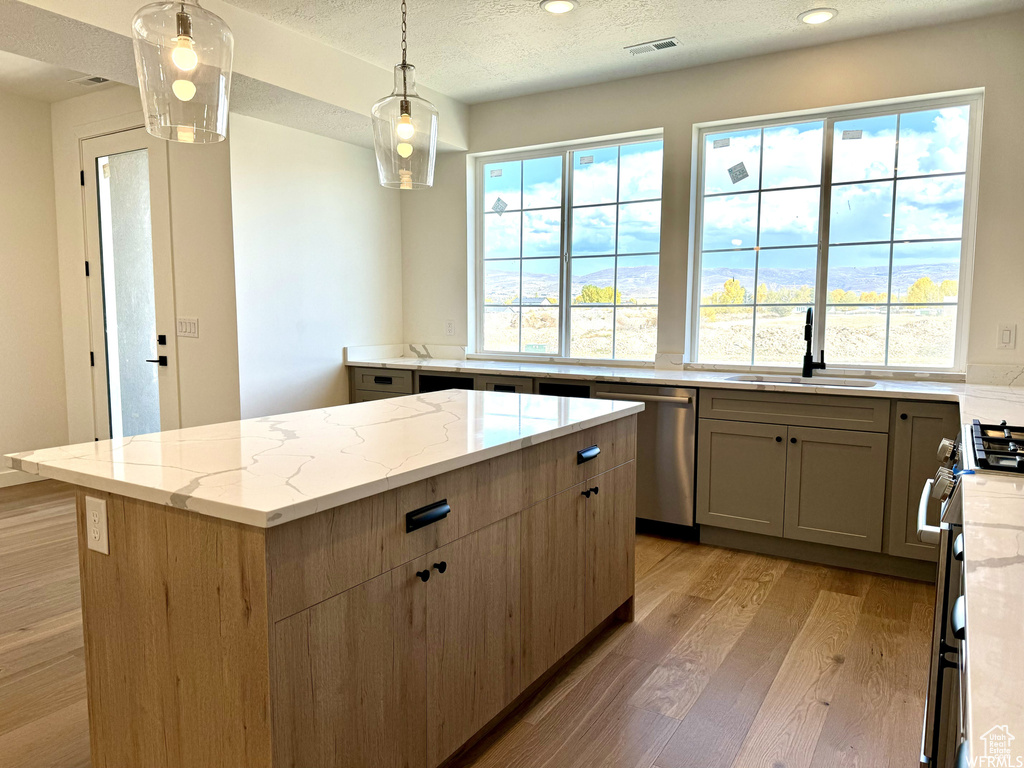 Kitchen featuring light stone countertops, decorative light fixtures, light hardwood / wood-style flooring, sink, and a center island