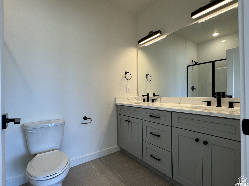 Bathroom featuring tile floors, toilet, double sink vanity, and a shower with door